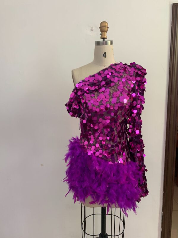 Vibrant purple sequin top with feathered trim displayed on a dress form, featuring an asymmetrical design and shiny embellishments, perfect for festive occasions or performance wear.