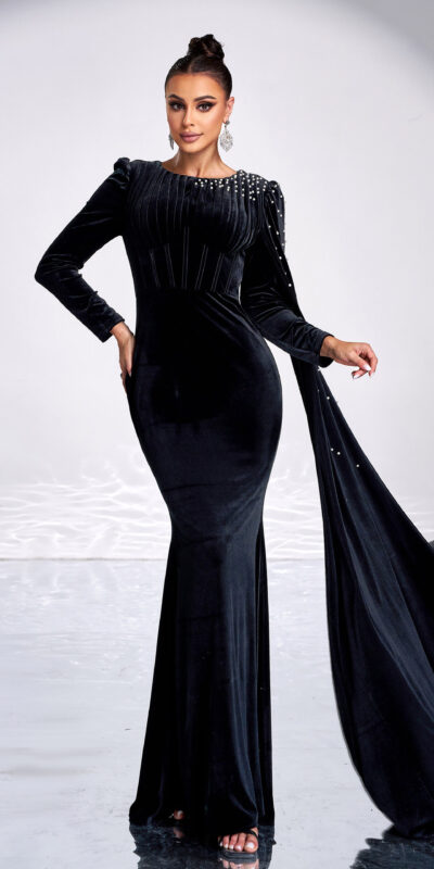 Elegant woman in a black velvet evening gown with long sleeves and embellishments, posing confidently in a reflective setting with rocks. The dress features a fitted silhouette and a dramatic train, perfect for formal occasions.