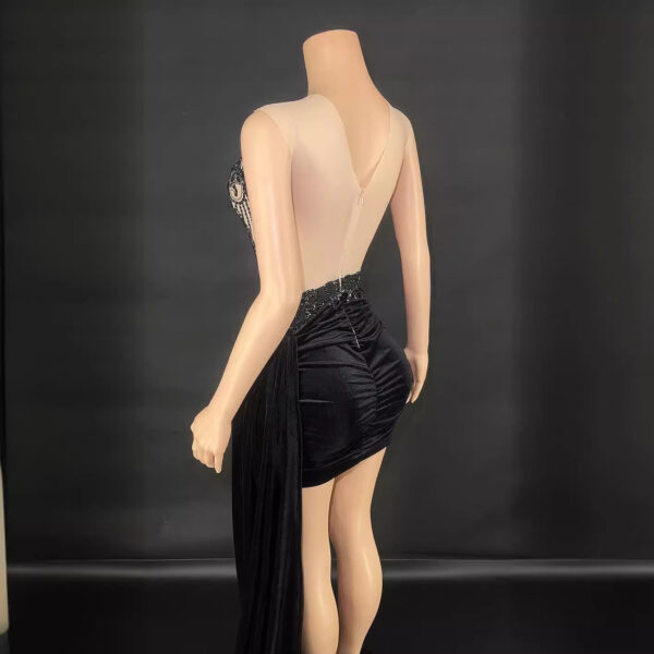 Elegant black evening dress with a sheer back and embellished details, showcased on a mannequin against a dark background. The dress features a fitted silhouette with a draped skirt and intricate beadwork on the bodice.