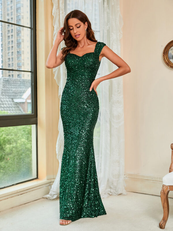 Elegant woman wearing a sparkling green evening gown with a fitted silhouette, standing gracefully in a well-lit room with large windows. The dress features cap sleeves and a sweetheart neckline, showcasing its glamorous design.