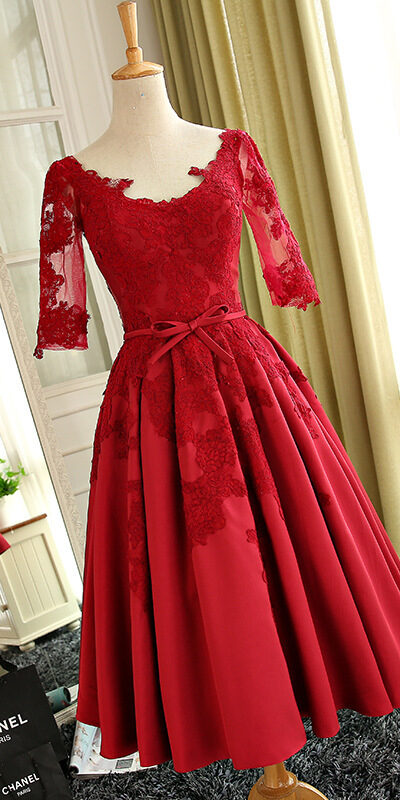 Elegant red lace dress with three-quarter sleeves and a fitted bodice, featuring a flared skirt and a bow detail at the waist, displayed on a mannequin in a stylish interior setting.