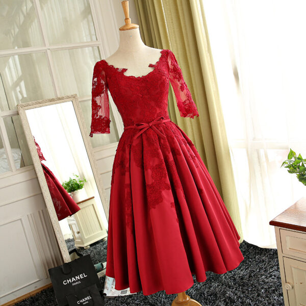 Elegant red lace dress with three-quarter sleeves and a fitted bodice, featuring a flared skirt and a bow at the waist, displayed on a mannequin in a bright, stylish room.