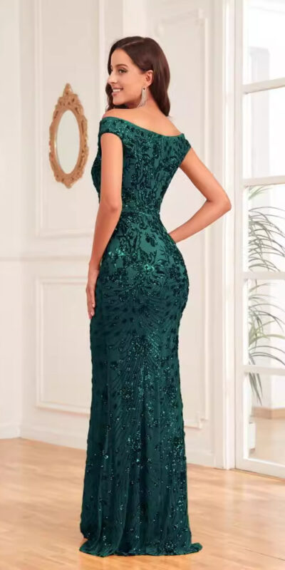 Elegant woman wearing a fitted emerald green off-the-shoulder evening gown, showcasing intricate beadwork and a flattering silhouette, posed in a bright, stylish interior.