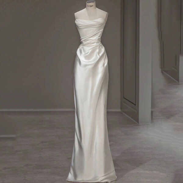 Elegant white satin evening gown featuring a strapless design with draped detailing and a fitted silhouette, displayed on a mannequin in a modern setting. Perfect for formal occasions and weddings.