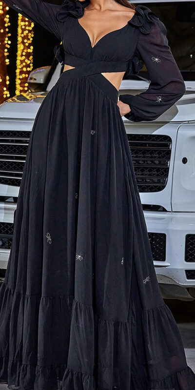 Woman posing in a long black dress in front of a white luxury SUV.