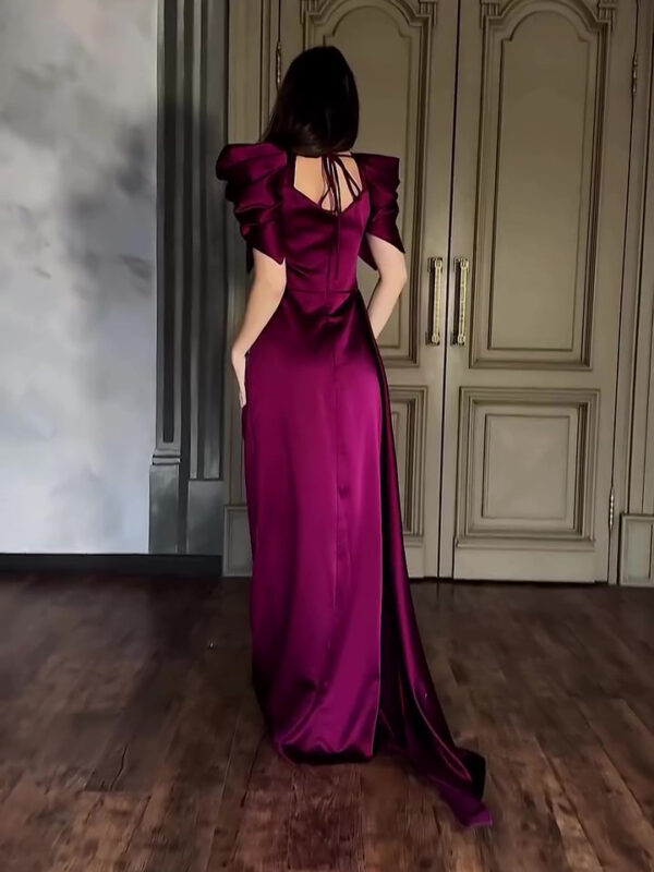 Elegant woman wearing a deep burgundy evening gown with puffed sleeves, showcasing a sophisticated back design, set against a stylish interior with wooden flooring and ornate doors.