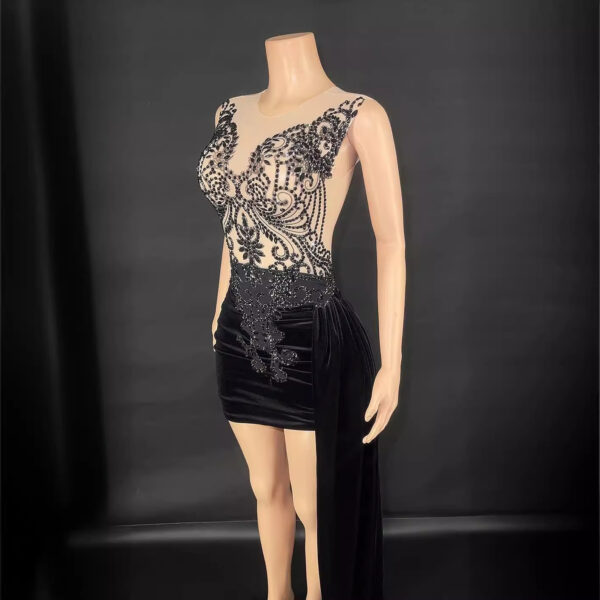 Elegant black evening dress featuring intricate beadwork and a fitted silhouette. The design includes a sheer bodice with ornate detailing and a velvet skirt with a dramatic side drape, perfect for formal occasions and special events.