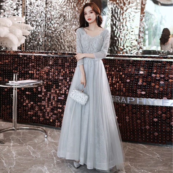 Elegant woman in a shimmering silver gown with intricate detailing, holding a sparkling handbag, poses in a stylish interior with a mirrored backdrop. Perfect for formal occasions and evening events.