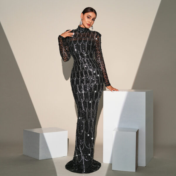 Elegant woman wearing a black sequined evening gown with a high neckline and long sheer sleeves, posing against a minimalist backdrop with geometric white pedestals. The dress features intricate beading and a fitted silhouette, highlighting her graceful pose and statement earrings.