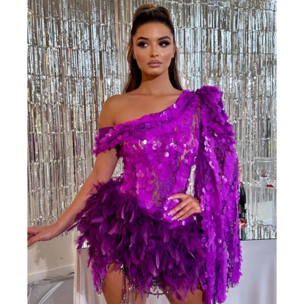 Model in a vibrant purple dress adorned with sequins and feathers, posing against a shimmering silver backdrop, showcasing a stylish one-shoulder design.