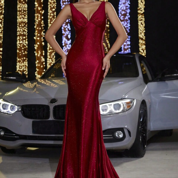 Woman in a red evening gown standing in front of a silver car with illuminated headlight, surrounded by decorative lights.