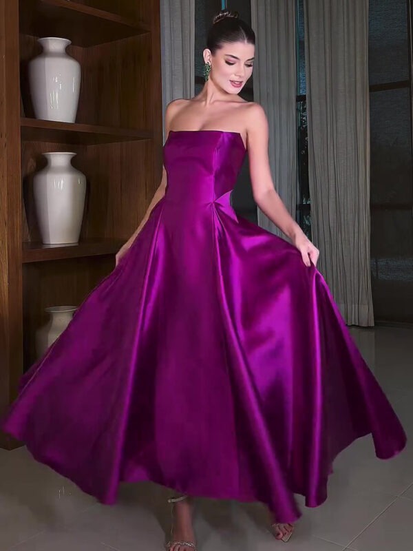 Model in a stunning strapless purple satin gown, twirling gracefully in an elegant indoor setting with wooden shelves and decorative vases. The dress features a full skirt and a fitted bodice, complemented by statement earrings and stylish sandals.