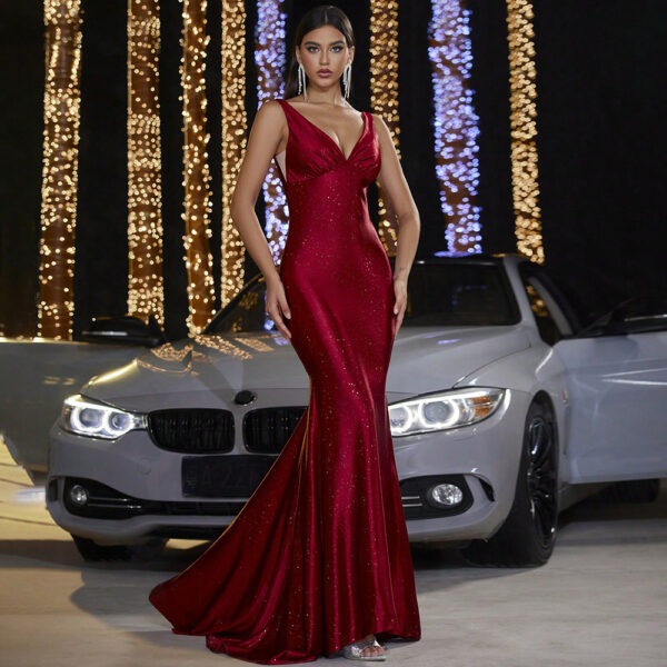 Elegant woman in a shimmering red evening gown poses confidently in front of a sleek silver car, surrounded by twinkling lights. The dress features a deep V-neckline and a fitted silhouette, perfect for formal occasions.