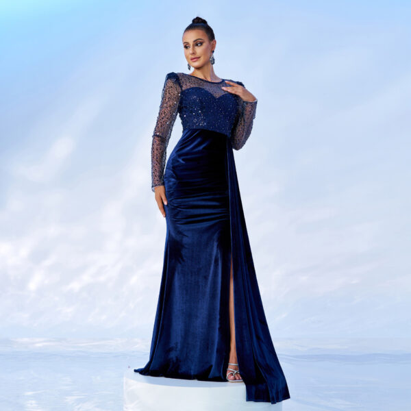 Elegant woman wearing a long navy blue evening gown with sheer embellished sleeves and a thigh-high slit, posing against a light blue background.