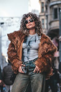 Fashionable woman wearing fur coat and sunglasses in urban street setting, exuding confidence.