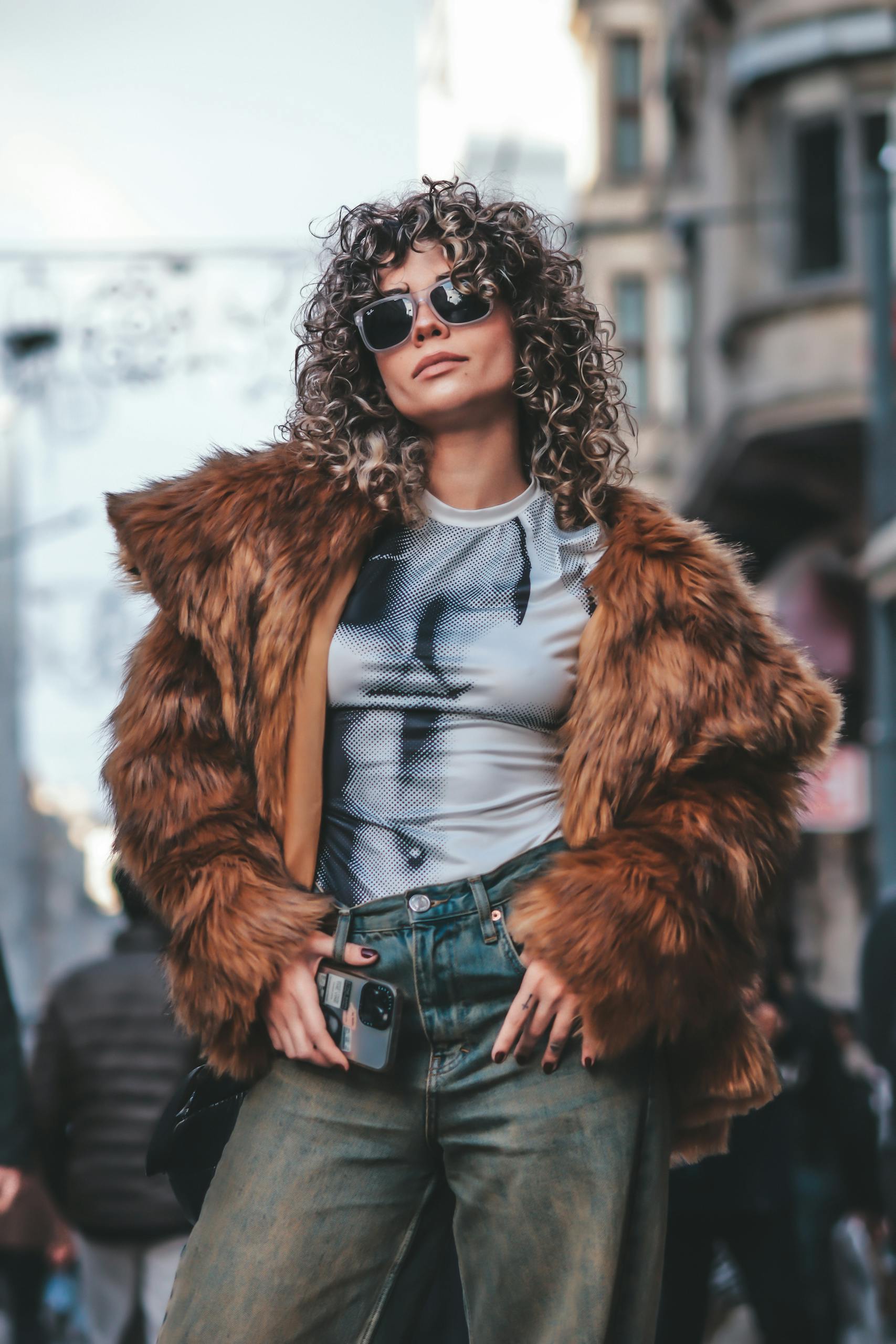 Fashionable woman wearing fur coat and sunglasses in urban street setting, exuding confidence.