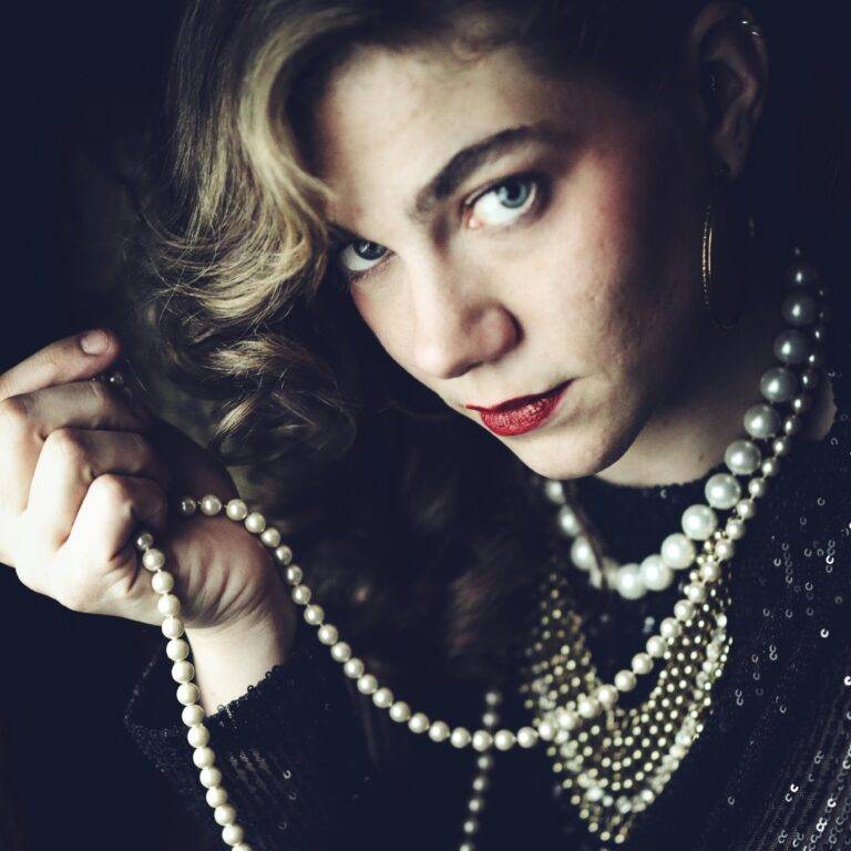 A woman with vintage styling holds a pearl necklace, exuding elegance and sophistication.