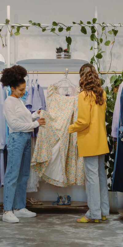 Two women shopping for trendy outfits in a modern clothing boutique filled with colorful garments.