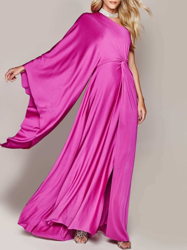 Woman wearing a vibrant pink one-shoulder gown with a flowing cape sleeve and silver sandals.