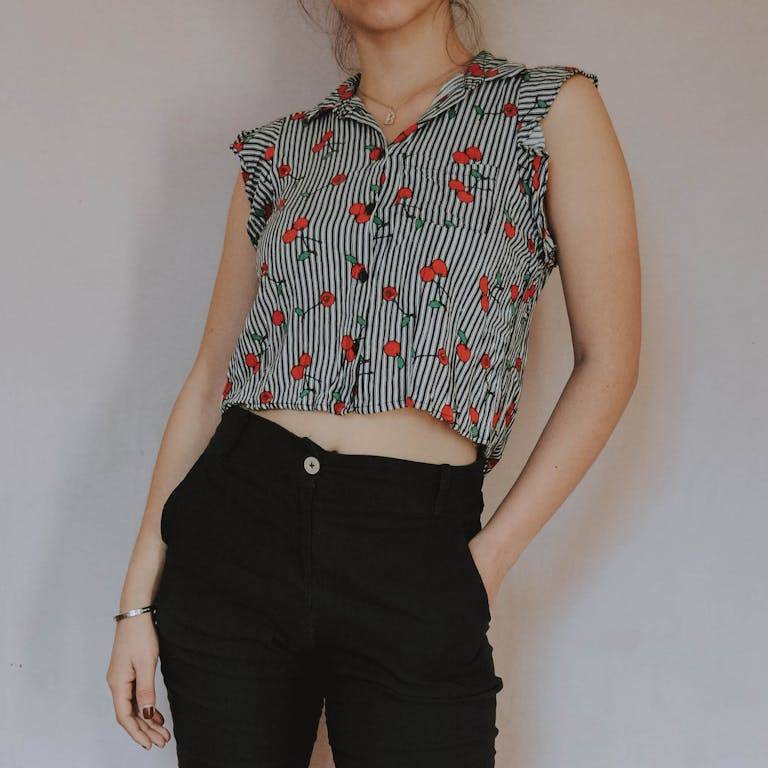 Young woman modeling a cherry print blouse with black pants, showcasing modern casual fashion.